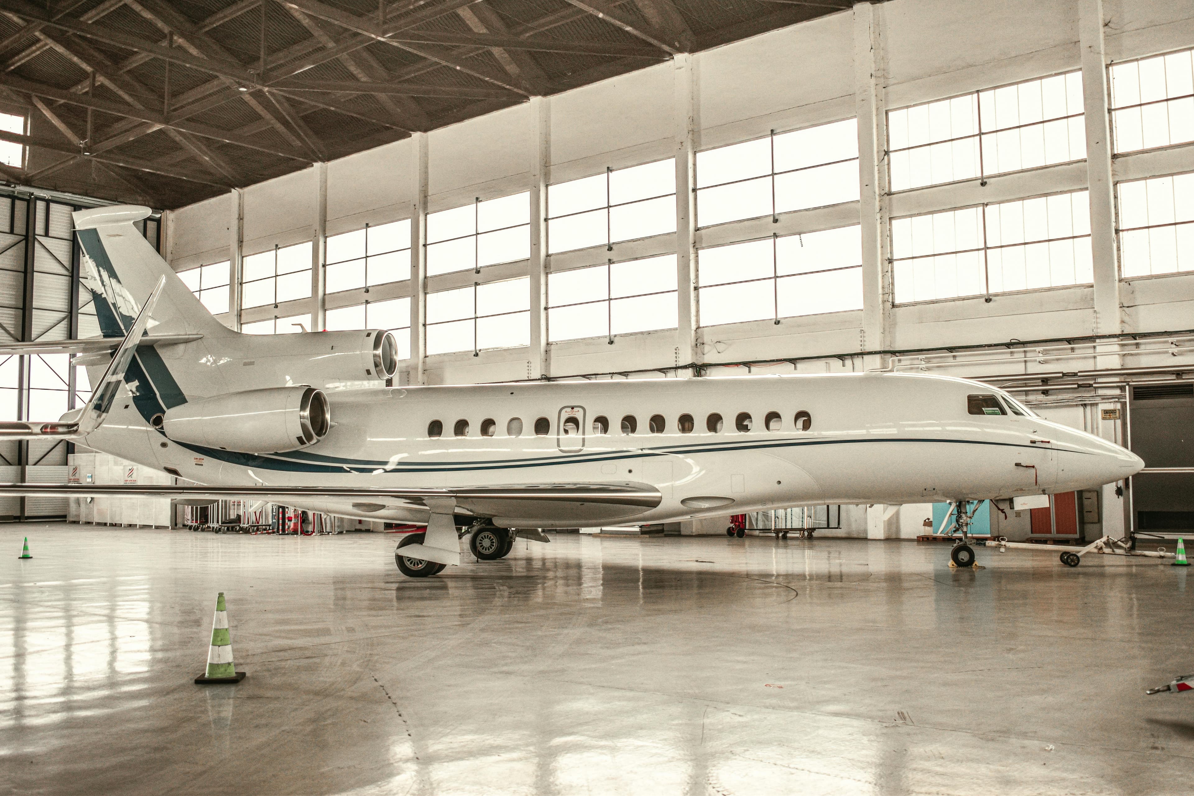 A midsize private jet parked on the FBO ramp at Hanscom Field with New England trees in the background under an overcast spring sky