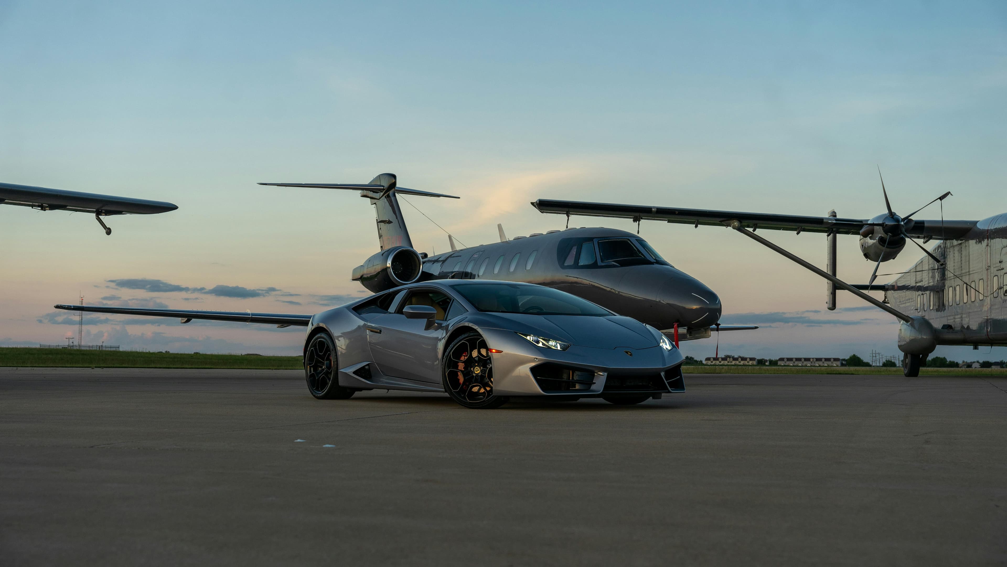 A midsize private jet parked on an FBO ramp at dusk with baggage cart alongside, lit cabin windows visible
